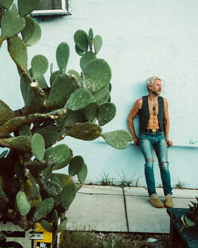Standing against a sunlit wall beside towering cactus